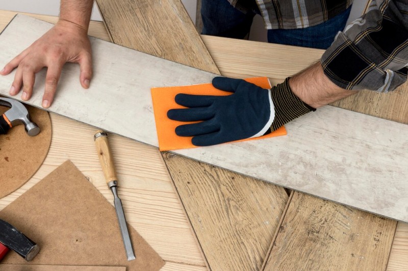 Man sanding a wooden plank with glove and sponge on a workbench